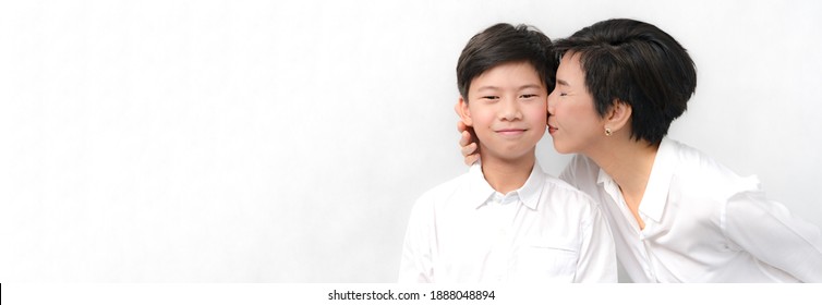 Banner Portrait Of A Beautiful Middle Aged Asian Mother Gently Kiss Her Preteen Son With Love And Happiness. Parenting Child, Beloved Son, Mother's Day, Teen Boy And Mom, Precious Moment, Bonding.