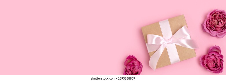 Banner with present with a tied ribbon and heads of rose flower on a pink pastel background. Romantic composition with gift. - Shutterstock ID 1893838807