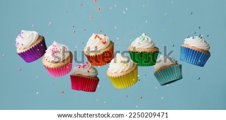 Banner with row of tumbling colorful rainbow cupcakes with falling sugar sprinkles