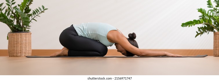 Banner Side view of Asian woman wearing green sportwear doing Yoga exercise,Yoga Child’s pose or Balasana,Calm of healthy young woman breathing meditation with yoga at home,Exercise for wellness life