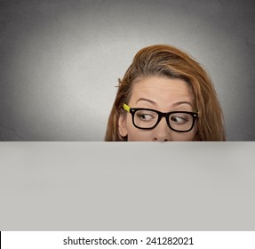 Banner Sign Woman Peeking Over Edge Of Blank Empty Paper Billboard. Beautiful Young Girl With Glasses Looking To Side Surprised Curious Scared Funny Interested Open Eyes Isolated Grey Wall Background