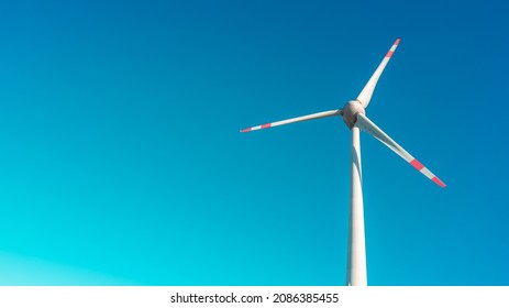 Banner with a solitary big wind turbine to generate electrical power as green eco friendly energy at blue turquoise deep sky and copy space background. Concept of sustainable clean industry and life