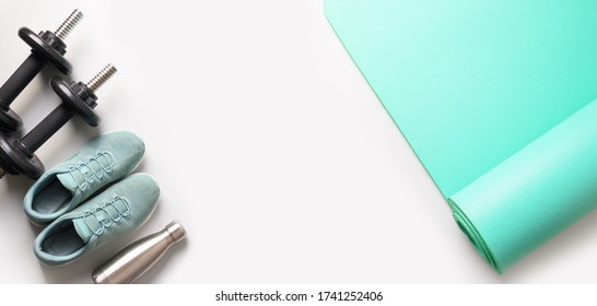 Banner of sport and fitness equipment, dumbbells, yoga mat, shoes, water bottle on grey. View from above, space for your text.