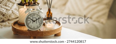 Banner. Spring change, Daylight Saving Time concept. White alarm clock, bulbous flowers, candles on the white table. Cozy home interior. Copy space