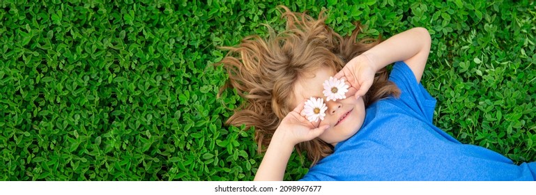 Banner With Spring Child Face. Spring Kid. Happy Child Enjoying On Grass Field And Dreaming. Funny Little Boy With Daisy In Eyes. Kids On Green Grass Background.