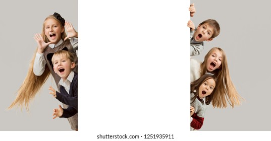 Banner with a surprised children peeking at the edge with copyspace. The portrait of cute little kids boy and girls looking at camera against white studio wall. Kids fashion. Sublings day. 