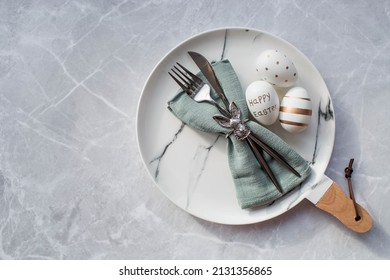 Banner. Table Setting. A Fashionable Marble Plate With A Rabbit On A Napkin, Easter Eggs And Feathers On A Gray Background. Top View. Happy Easter Holiday Concept For Cafes And Restaurants.