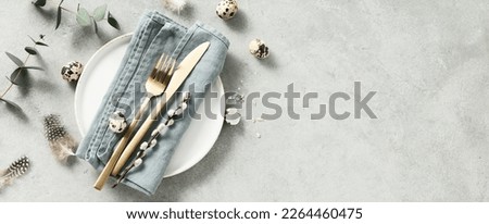 Banner. Table setting. A fashionable minimalistic plate with a linen napkin, Easter eggs and feathers on a gray background. Top view. Happy Easter holiday concept for cafes and restaurants. Copy space