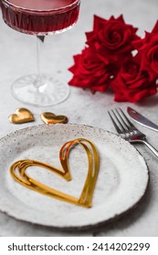 The banner. Table setting. Stylish ceramic plate, glass of red wine, red roses, fork and golden hearts on a concrete background. The concept of celebrating Valentine's Day for cafes and restaurants.