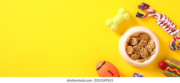 Banner template for pet store. Bowl with dog food, rope, bone, ball on yellow background. Flat lay, top view. - Shutterstock ID 2311547611