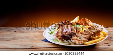 Banner with a traditional Greek mixed grill platter served with tomato rice, French Fries and cool refreshing raiti yogurt on a rustic table with copy space