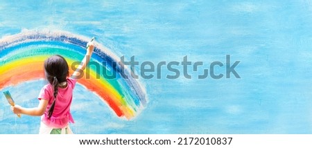 Banner of unidentified little girl is painting the colorful rainbow and sky on the wall and she look happy and funny, concept of art education and learn through play activity for kid development.