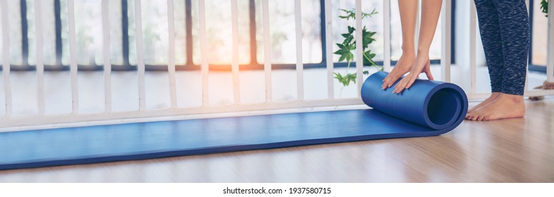Banner Woman hands rolled up yoga mat on gym floor in yoga fitness training room. Home workout woman hands rolling foam yoga gym mat background. Panoramic Woman barefoot home workout with copyspace