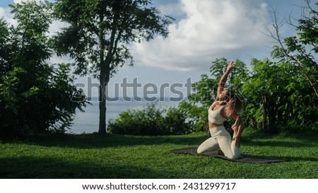 Banner of a young athletic Latino woman in a tracksuit performs yoga on a cliff near the ocean coast. Yoga practice in nature, wellness treatments for body and mind. Charming woman goes in for sports.