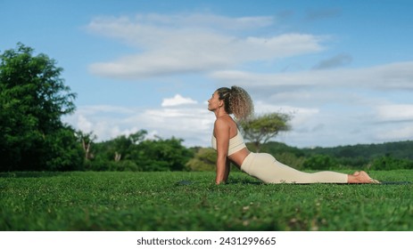 The banner of a young attractive Latino athletic woman is doing yoga outdoors on a mat against the backdrop of a green forest and breathing deeply. A yoga trainer performs asana in the park at dawn - Powered by Shutterstock