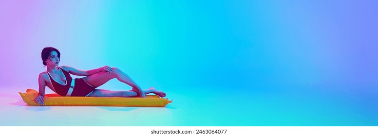 Banner. Young attractive woman in retro swimsuit posing lying on inflatable in neon light against vibrant gradient background. Copy space. Concept of summer holidays, traveling, fashion, vacation. Ad - Powered by Shutterstock