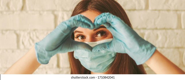 Banner junge Frau in Schutzmaske und medizinische Handschuhe, die das Zeichen der Liebesform tragen. Fröhliches Mädchen in medizinischer Gesichtsmaske und Handschuhe, die durch Hände in Form von Herzensymbol schauen. Gesundheitswesen, COVID-19