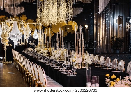 Banquet decoration in hall restaurant. Festive tables with flower composition on black tablecloth and chairs for guests. Wedding set up, dinner table reception in area on party. Setting. Side view.