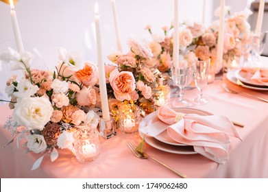 Banquet, restaurant. Table setting. Pink plates, gold cutlery, glasses. On the table is a pink tablecloth. Peach-colored napkin with a golden ring. Floral arrangements in peach pink hues. Tall candles - Powered by Shutterstock