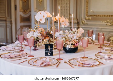 banquet tables with white tablecloths are in the hall of the old house, on the tables are flower arrangements, candles, plates with napkins, glasses and cutlery