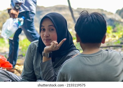 BANTEN, INDONESIA - MAY 7, 2022: Close Up Of A Young Asian Muslim Woman Looking At The Camera Wearing A Black Headscarf Sitting Cheerfully With A Small Child. Family Picnic On Pulo Manuk Beach, Banten