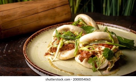 Bao buns with chicken and greens sauce on a plate dish and wooden backgroound