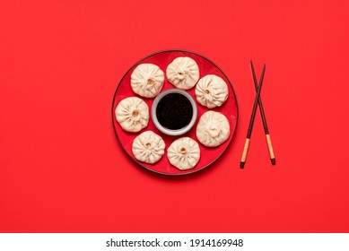 Bao dumplings on red plate with Chinese sauce, isolated on a red background. Steamed pork baozi, homemade xiao long bao, top view. Steamed buns.