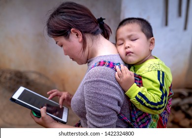 Bao Loc, Lam Dong Province, Vietnam - Jun 2, 2019: The Image Of A Woman Holding A Small Baby On Her Back While Her Hand Is Still Working With The IPad In Bao Loc, Lam Dong Province, Vietnam