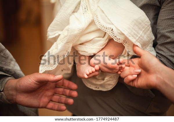 The baptism of a child. The godfather holds the\
child in his arms. Closeup photo, priest and godmother stretch\
hands to baby legs\
