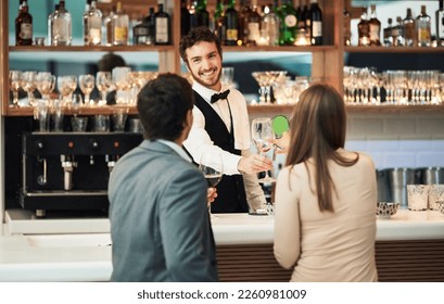 Bar, barman and serve a couple alcohol drinks on a date with hospitality, happy and smile at a hotel. Waiter, bartender and server help customers or people with good service for a celebration