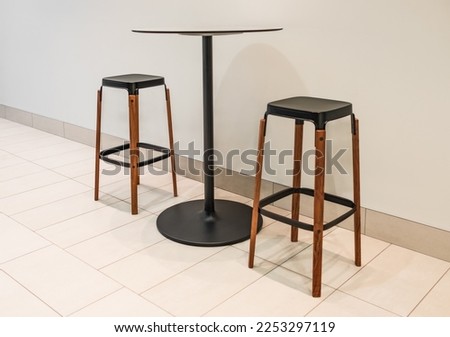 Bar chairs and round table in cafe. Round coffee table with steel base and two tall stools. Tall table steel legs simplistic, tall wooden bar stools. Nobody, selective focus