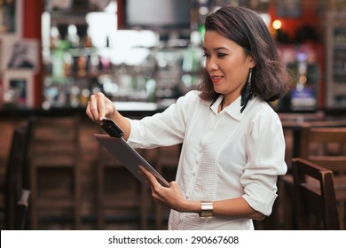 Bar Owner Using Credit Card Reader On The Tablet To Swipe Payment