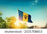 Barbados national flag waving in blue sky behind the tree and building. The flag blowing with beautiful sunlight. Barbados national flag for independence day.