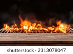 barbecue BBQ grill with flaming fire and ember charcoal on black background, wooden table