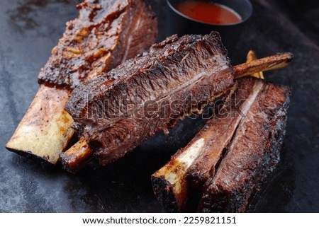 barbecue burnt chuck short beef ribs marinated with spicy rub and served with a hot chili sauce as close-up on a rustic board 