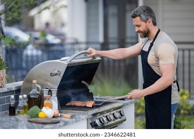 Barbecue concept. Middle aged hispanic man in apron for barbecue. Roasting and grilling food. Roasting meat outdoors. Barbecue and grill. Cooking meat in backyard. - Powered by Shutterstock