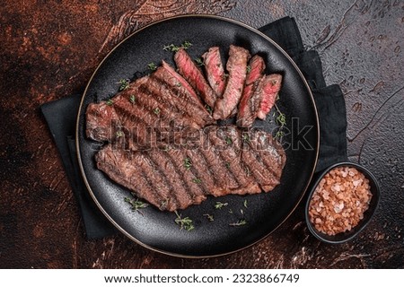 Barbecue denver strip beef meat steak on a plate. Dark background. Top view.