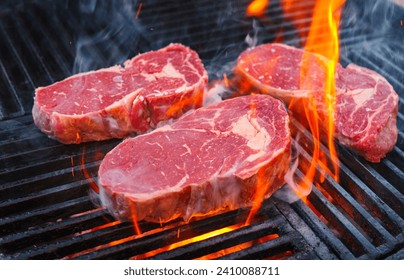 Barbecue dry aged angus rib-eye beef steak grilled as close-up on a charcoal grill with fire and smoke  - Powered by Shutterstock