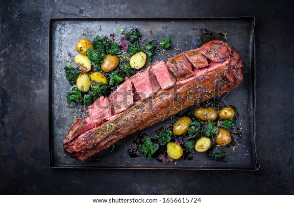 Barbecue dry aged venison tenderloin fillet steak\
and saddle natural with kalette and fried potatoes offered as top\
view on a rustic board