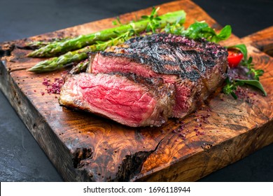 Barbecue dry aged wagyu entrecote beef steak with lettuce and green asparagus as closeup on an old rustic wooden cutting board 