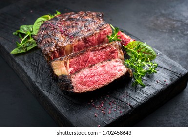 Barbecue dry aged wagyu entrecote beef steak roast with lettuce and salt as closeup on a charred wooden board 