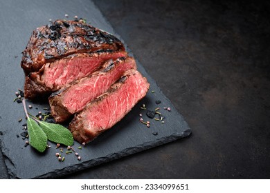 Barbecue dry aged wagyu rib-eye beef steaks with herb and black salt served as close-up on a black board with copy space right