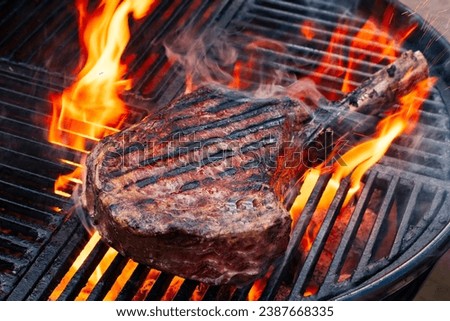Barbecue dry aged wagyu tomahawk steak offered as close-up on a charcoal grill with fire and smoke 