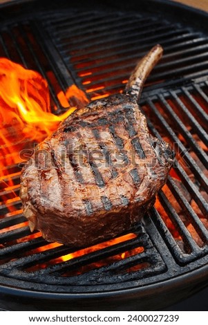 Barbecue dry aged wagyu tomahawk steak offered as close-up on a charcoal grill with fire and smoke 