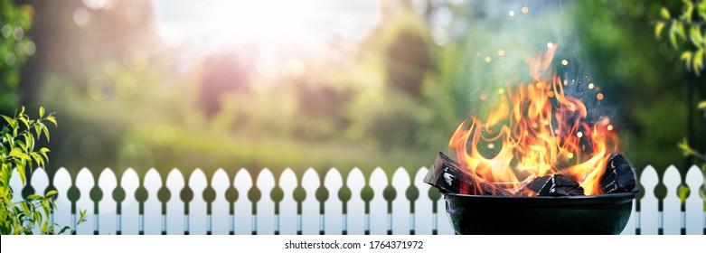 Barbecue Grill With Wood Fire In Backyard With Picket Fence And Sunset Background