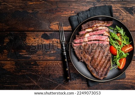 Barbecue grilled and sliced wagyu Rib Eye beef meat steak on a plate. Dark background. Top view. Copy space.