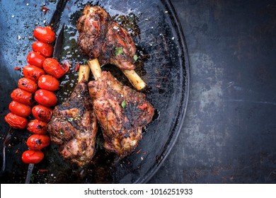 Barbecue leg of lamb and a tomato skewer as top view on a metal tray with copy space right 