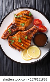 Barbecue Pork Chop In A Tamarind Sauce, With Lemon And Tomatoes Close-up On A Plate On The Table. Vertical Top View From Above
