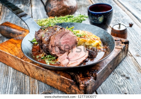 Barbecue roast boar joint with roesti\
and game red wine sauce as top view in a wrought-iron pan\
