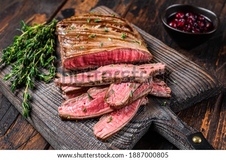 Barbecue sliced flank beef meat steak on a wooden cutting board. Dark wooden background. Top view.